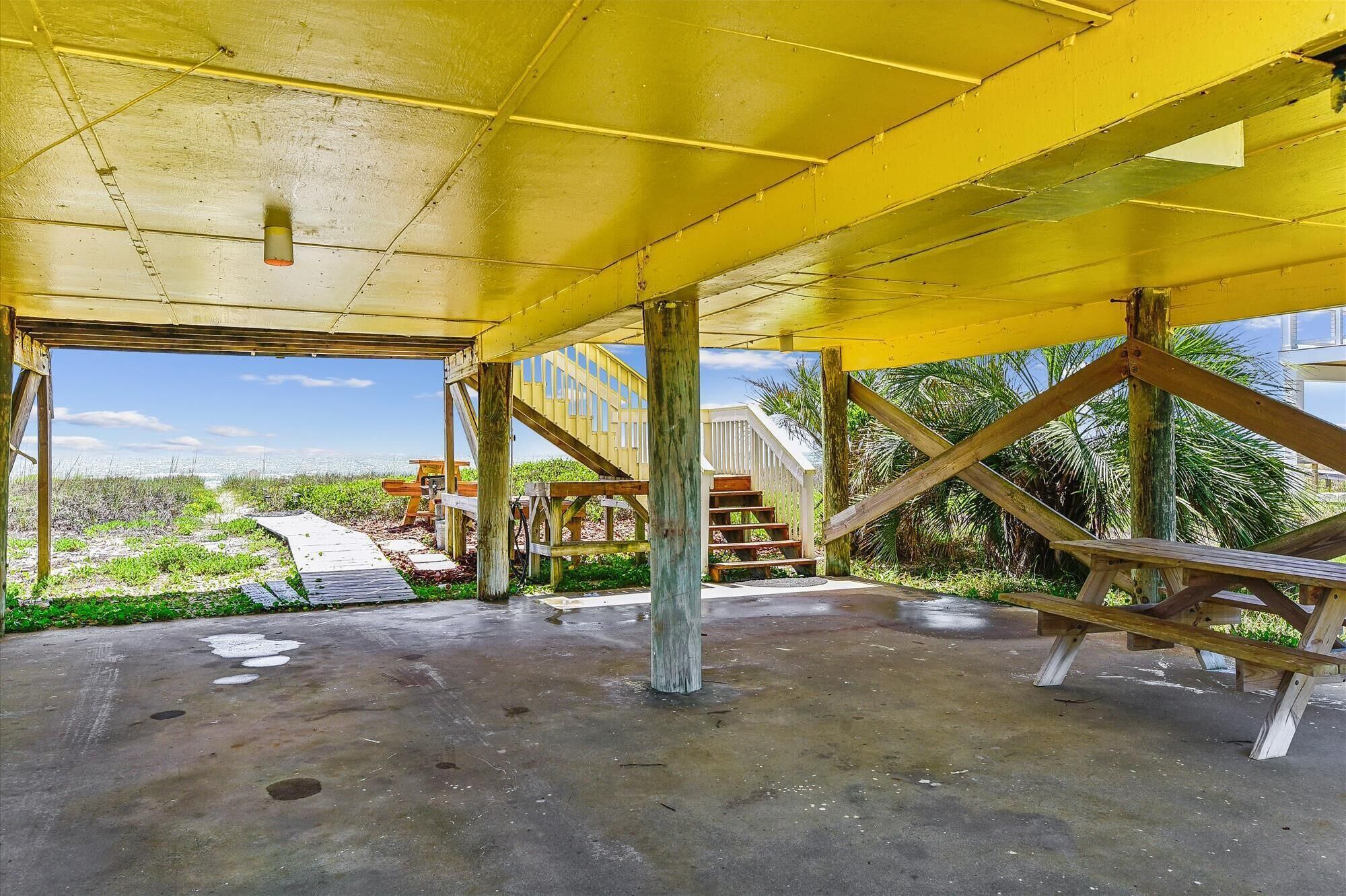 Une structure à ciel ouvert dotée d’un plancher en béton, de poutres en bois et d’un escalier menant à un niveau supérieur.