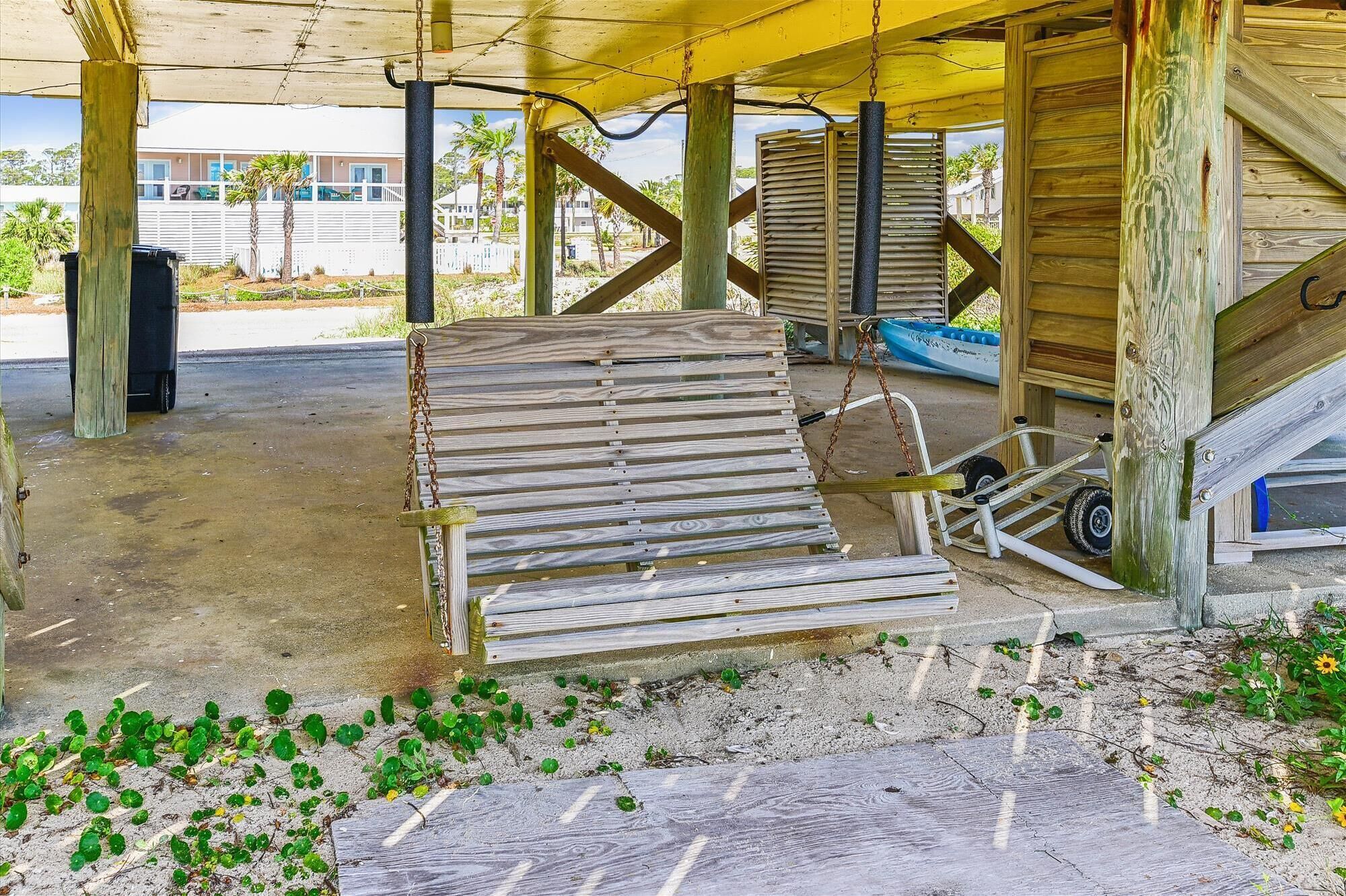 A wooden bench under a yellow canopy, surrounded by sand and small plants.