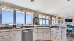 A kitchen with a large island, white cabinetry, and a view of the ocean. - You will delight in the fabulous gulf views from this elegant, Nantucket style beach home! (St. George Island)