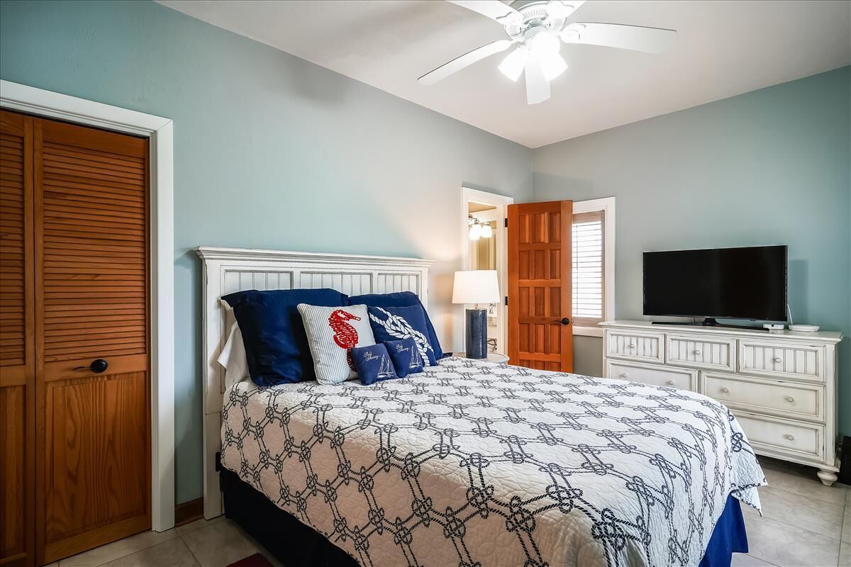A bedroom with a bed, a TV, a ceiling fan, and wooden doors.