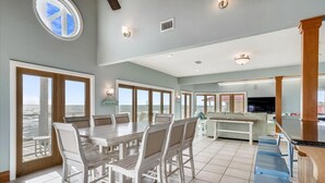 A spacious dining area with a large table and chairs, a bar area with stools, and large windows offering views of the ocean.