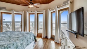 A bedroom with a bed, a TV, and a balcony with ocean views.