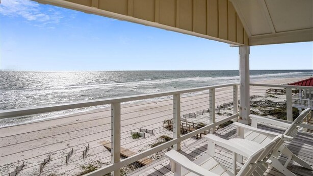 A beach view from a covered balcony with a railing, wooden deck, and a clear sky.
