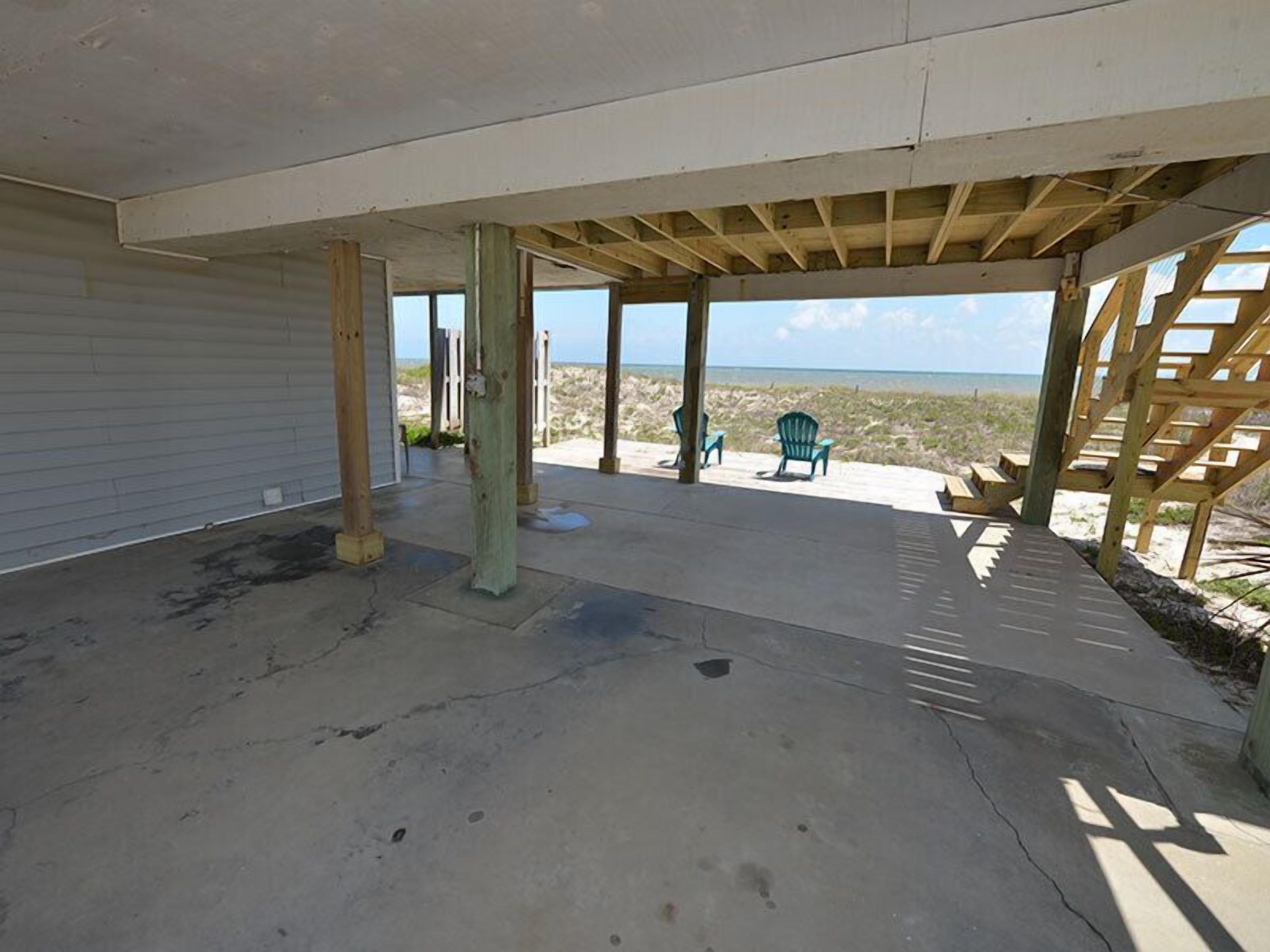 A covered outdoor area with concrete flooring, wooden pillars, and a view of the beach.