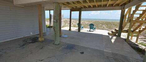 A covered outdoor area with concrete flooring, wooden pillars, and a view of the beach.