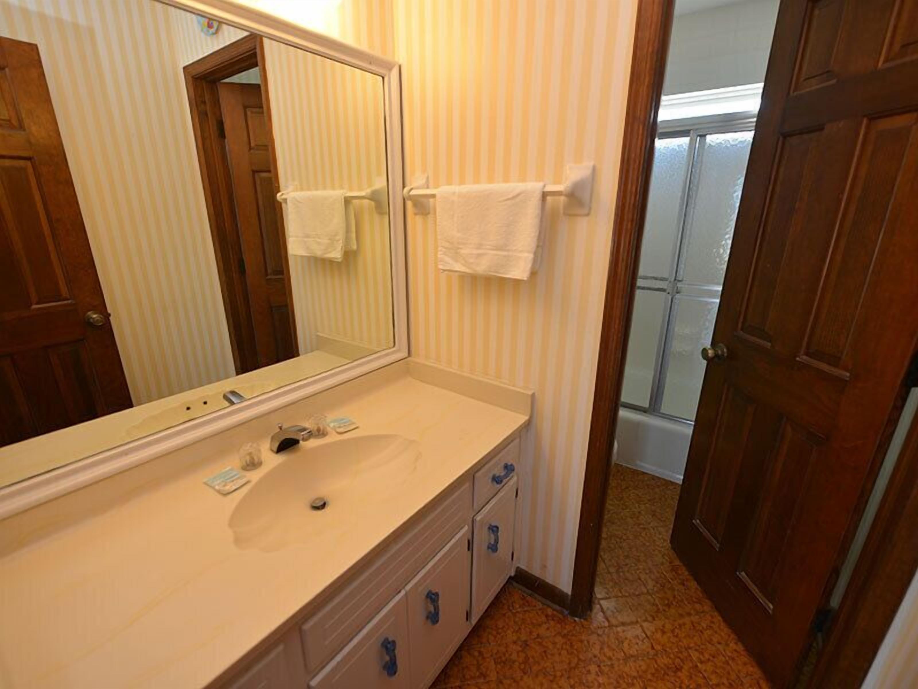 A bathroom with a large mirror, a sink, and two towel racks.