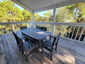 Une terrasse extérieure couverte, dotée d’une table et de chaises en bois, et entourée d’une balustrade blanche.