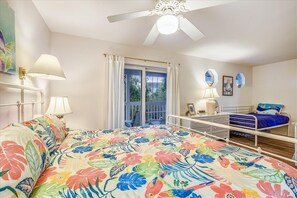 Une chambre à coucher comprenant un lit, un bureau, une chaise, un ventilateur de plafond et une fenêtre avec des rideaux.