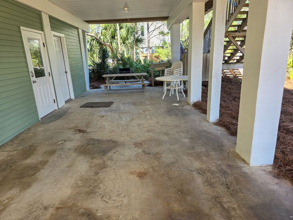 A covered patio area with a concrete floor, a wooden bench, and a table with chairs.