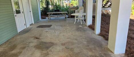 A covered patio area with a concrete floor, a wooden bench, and a table with chairs.