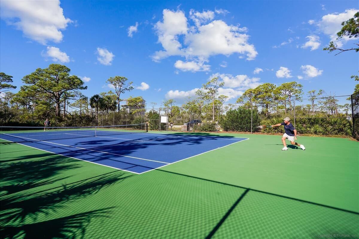 A tennis court with a net, surrounded by trees and a clear sky.