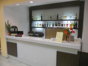Un espace bar avec un comptoir blanc, des étagères remplies de différentes bouteilles, une plante en pot et un présentoir à menus.