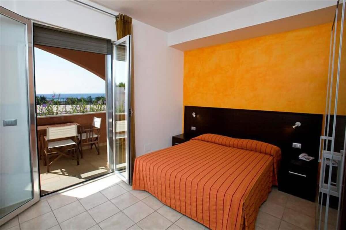 Une chambre comprenant un lit, une table de chevet, un bureau avec des chaises et une porte-fenêtre coulissante donnant sur un espace extérieur.