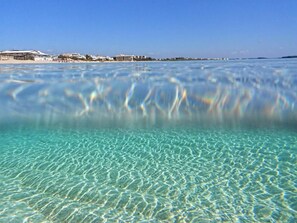 Ein freier Blick auf einen Strand mit ruhiger See und einer fernen Küstenlinie mit Gebäuden.