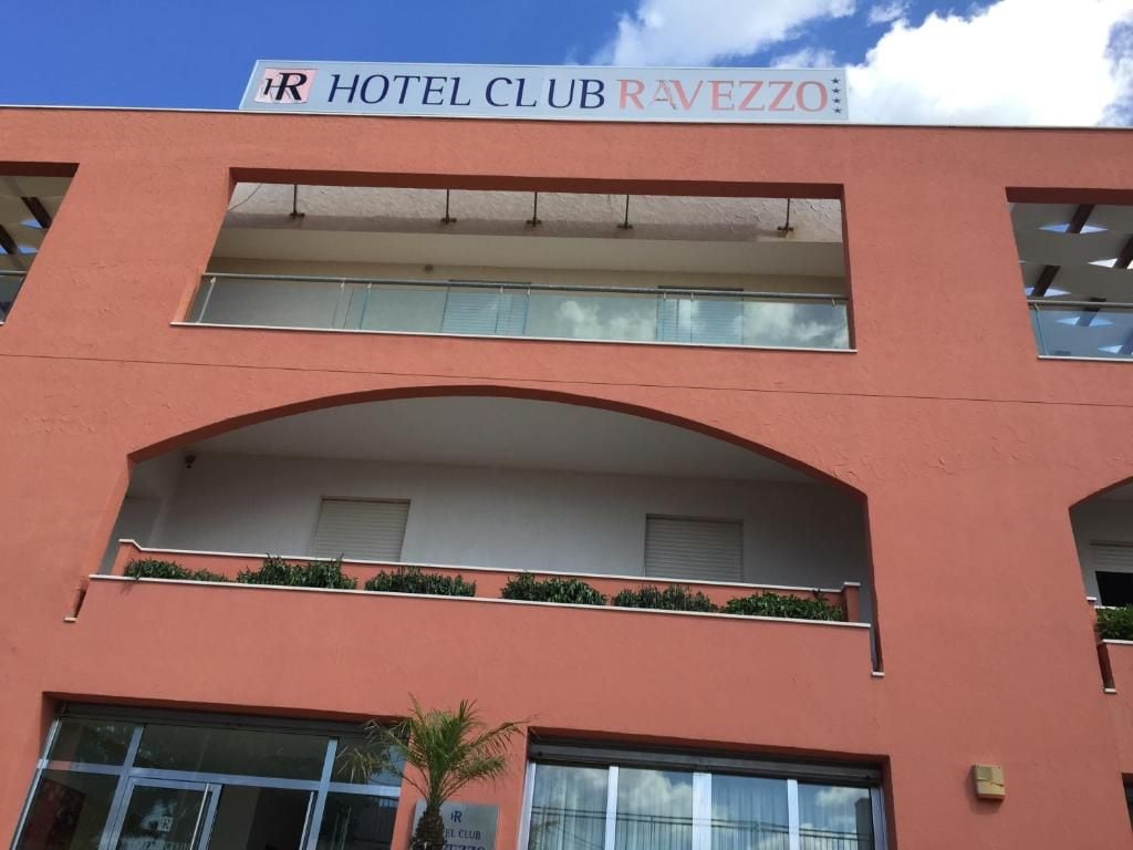 Un bâtiment d'hôtel avec une enseigne indiquant « HÔTEL CLUB RAVEZZO » et un balcon orné de plantes.