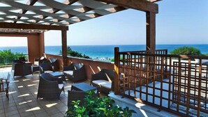 A covered outdoor seating area with wicker furniture and a view of the sea. - Hotel Club Ravezzo (Ugento)