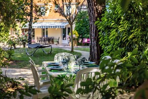 An outdoor dining area with a table set for four, surrounded by greenery and a building in the background.