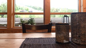 A wooden table with a dark rug, a chair, and two decorative vases. Large windows offer a view of a parking lot and greenery outside. - Trolltun Hotel (Dovre)