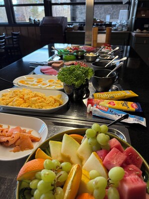 Een buffet met diverse gerechten, waaronder eieren, ham, kaas en fruit zoals druiven en watermeloen.
