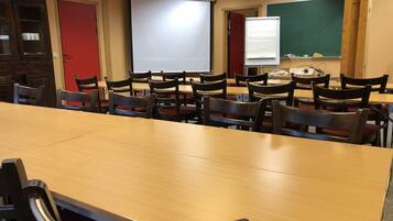 Un aula con mesas y sillas de madera, una pantalla de proyector, una pizarra y una pizarra de tiza.
