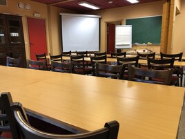 Un aula con mesas y sillas de madera, una pantalla de proyector, una pizarra y una pizarra de tiza.