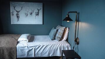 Un dormitorio con cama, almohadas, una mesita de noche, una lámpara de pared y una obra de arte con motivos de ciervo.