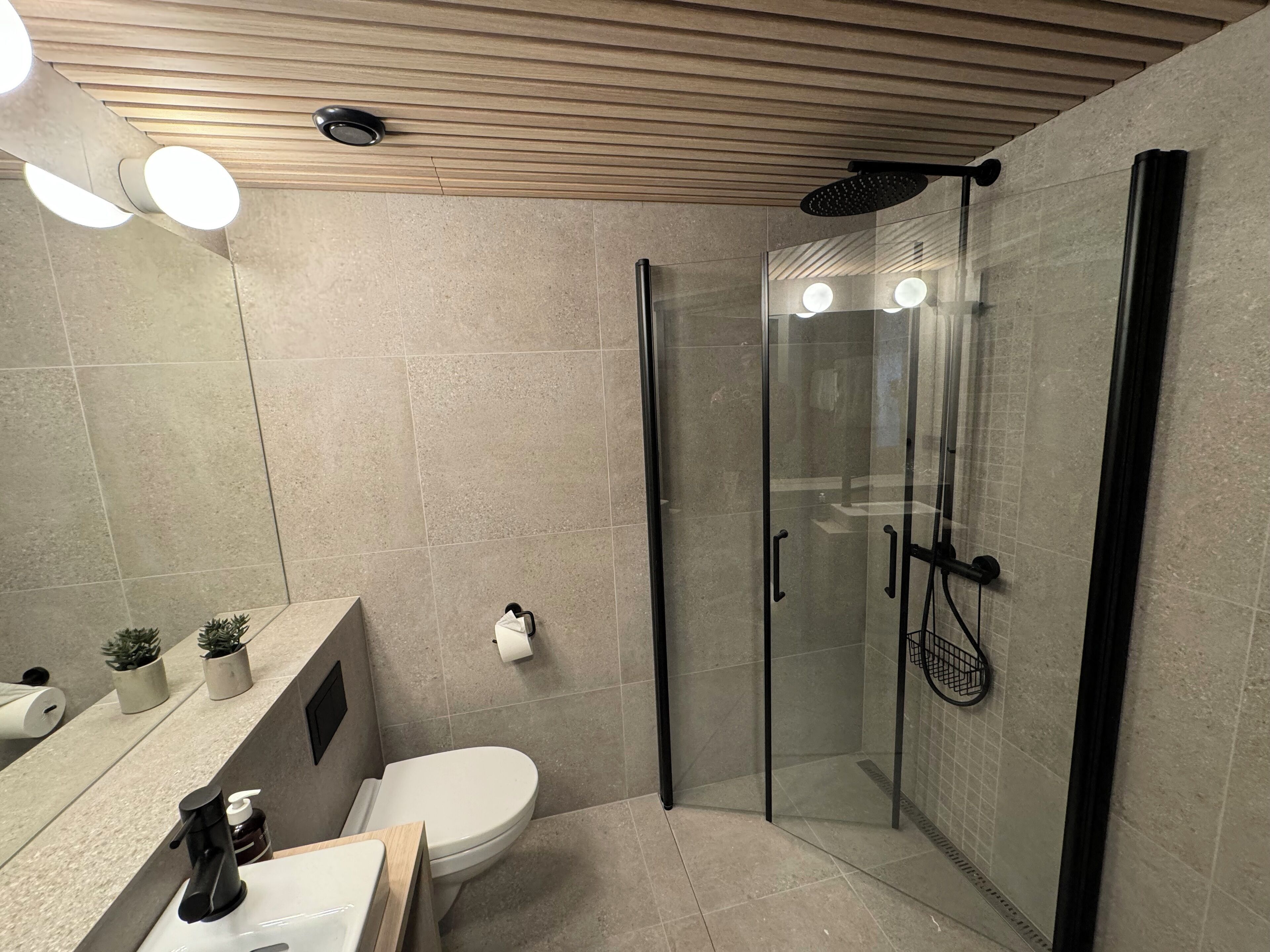 Une salle de bain moderne dotée d’une douche à parois de verre, de toilettes, d’un lavabo avec un miroir et d’un plafond équipé de spots encastrés.