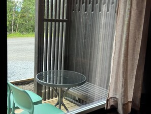Een glazen tafeltje met metalen frame, een groene plastic stoel en een houten hek op de achtergrond.