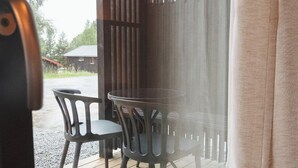 A wooden deck with a table and chairs, a window with vertical blinds, and a view of the outdoors. - Trolltun Hotel (Dovre)