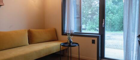 A room with a yellow sofa, a small table with a vase, and a window with curtains.