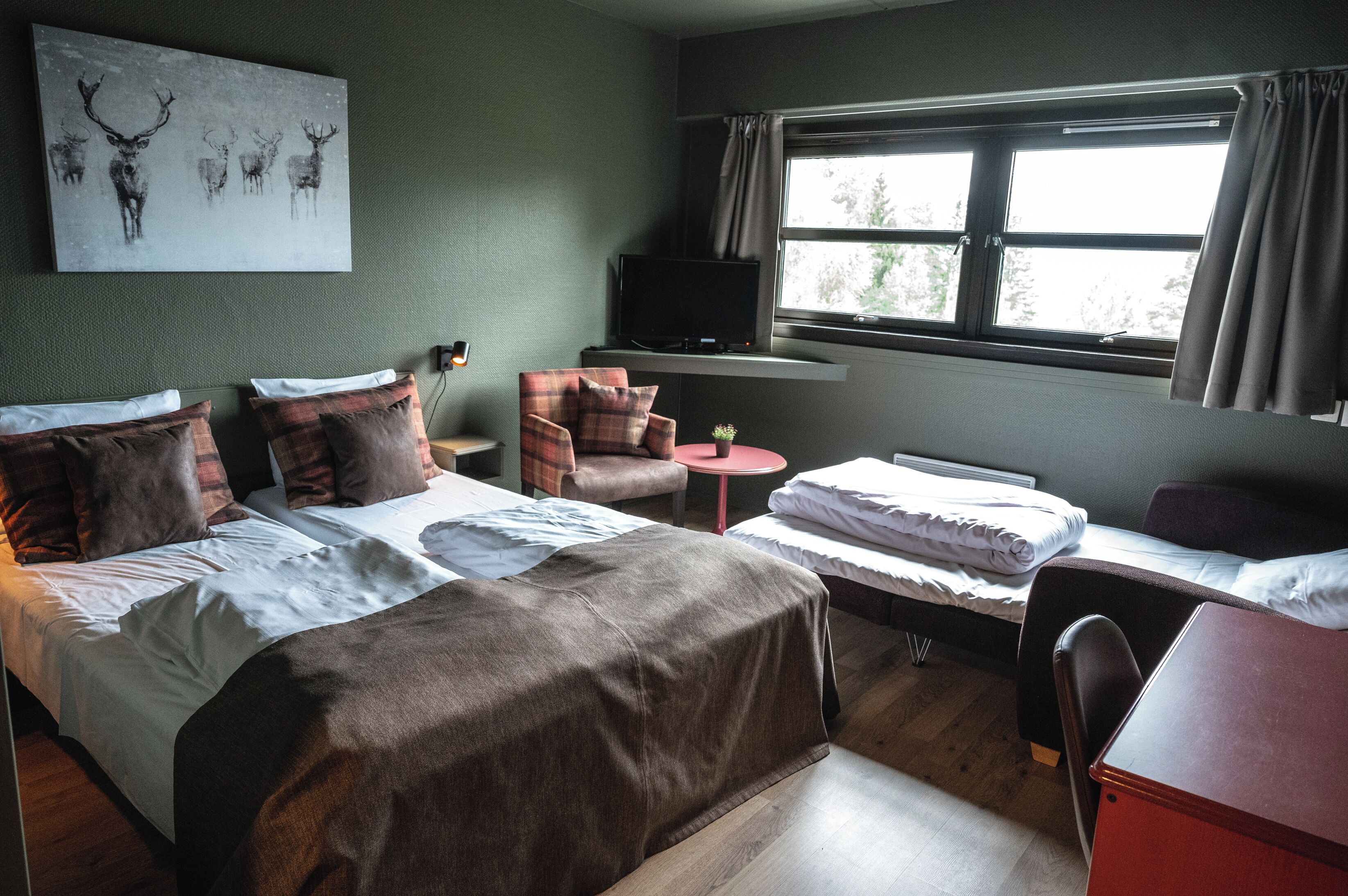 Une chambre d’hôtel équipée d’un lit, d’un bureau, d’une chaise, d’une télévision et d’une fenêtre avec des rideaux.