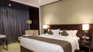 A hotel room with a large bed, bedside tables, a desk, and a lamp.