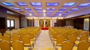 A conference room with rows of yellow chairs, a patterned carpet, and a ceiling with blue lighting.