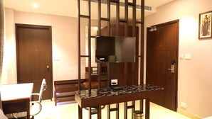 A hotel room with a wooden desk, a chair, a television mounted on a stand, and a door.