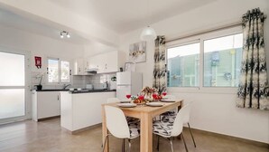 Eine moderne Küche mit weißen Schränken, einem Esstisch für vier Personen und einem großen Fenster mit Vorhängen.