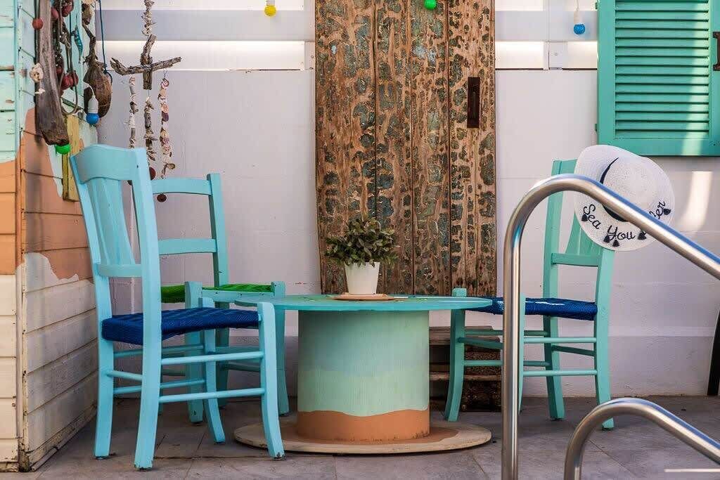 A small outdoor seating area with turquoise chairs and a round table, surrounded by a rustic wooden fence and a potted plant.