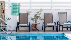 Ein Poolbereich mit drei Liegestühlen, einem kleinen Tisch mit einer Vase und zwei Gläsern Orangensaft sowie einer Wand-Klimaanlage.