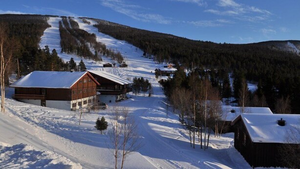 A snow-covered mountain village with wooden buildings and a ski slope. - Dombås Hostel (Dovre)