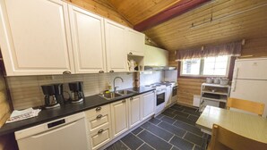 A compact kitchen with white cabinets, a dishwasher, a stove, and a sink. - Dombås Hostel (Dovre)