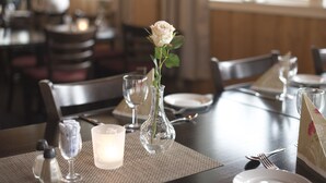 A dining table set with a clear glass vase containing a single rose, a candle, and a placemat. - Dombås Hostel (Dovre)