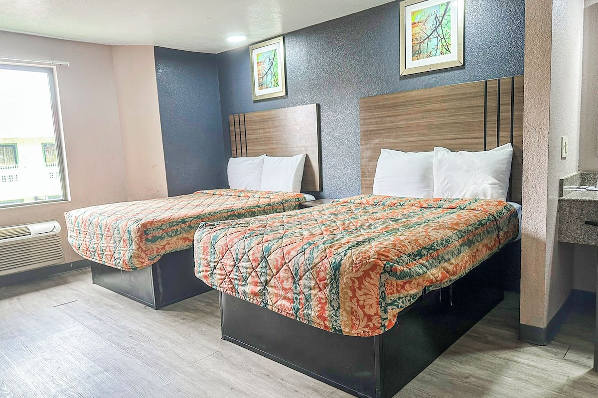 Habitación de hotel con dos camas, una ventana con persianas, un aire acondicionado instalado en la pared y un pequeño baño.