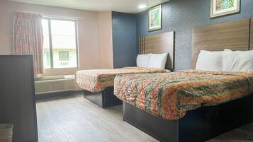 Quarto de hotel com duas camas, uma janela grande com cortinas, um aparelho de ar condicionado e uma obra de arte emoldurada na parede.