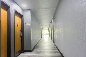 Un pasillo largo y estrecho con puertas de madera a la izquierda y un letrero que indica la habitación 222.