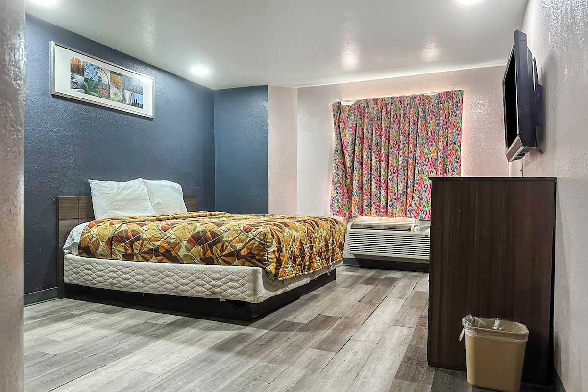 Un dormitorio con cama, televisor montado en la pared, ventana con cortinas y equipo de aire acondicionado.