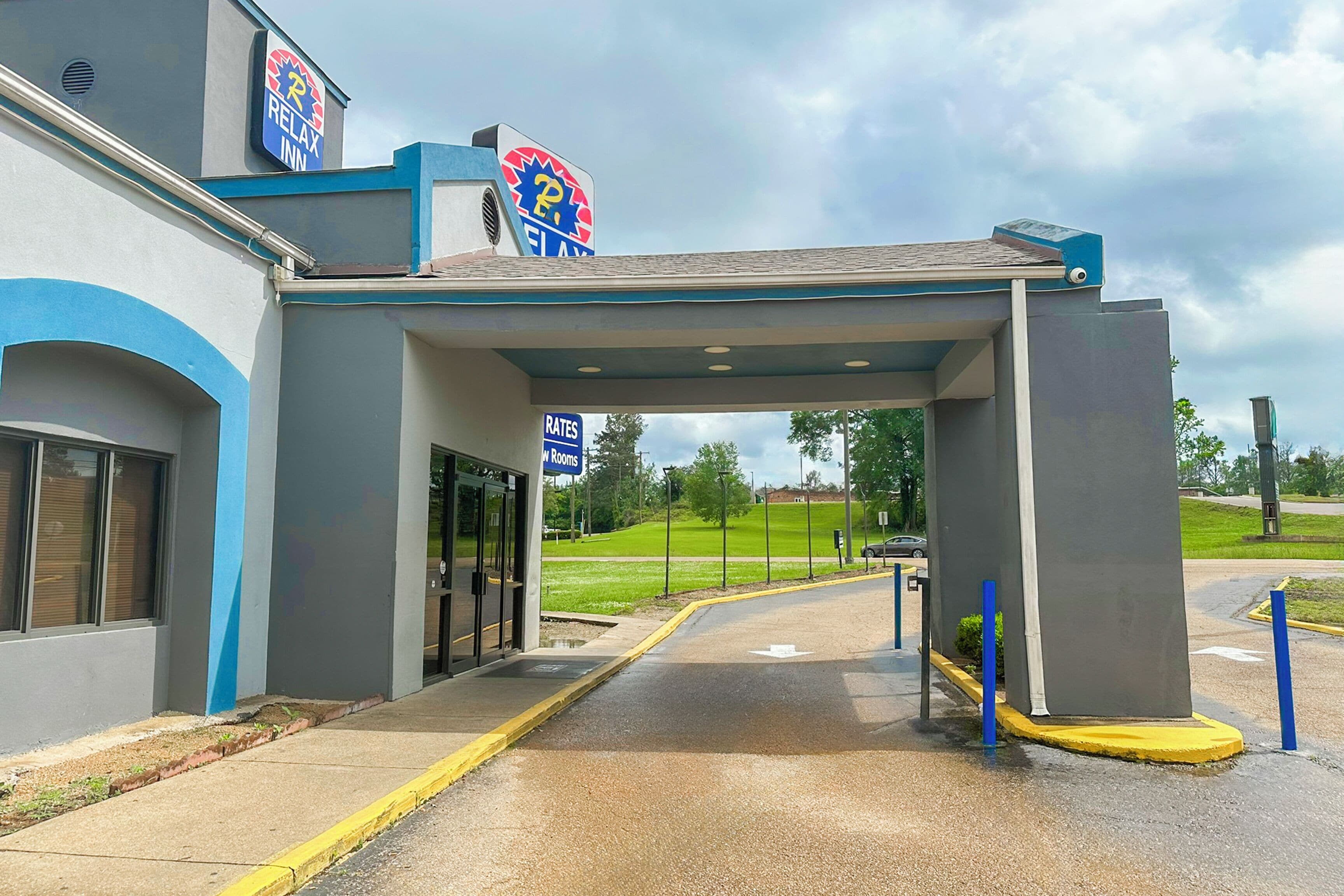 A hotel entrance with a covered walkway, a sign for 'Rates in Rooms', and a parking lot.