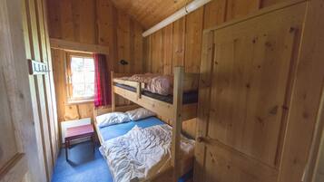 Une chambre dans un chalet en bois, avec des lits superposés, une petite table et une fenêtre avec des rideaux.