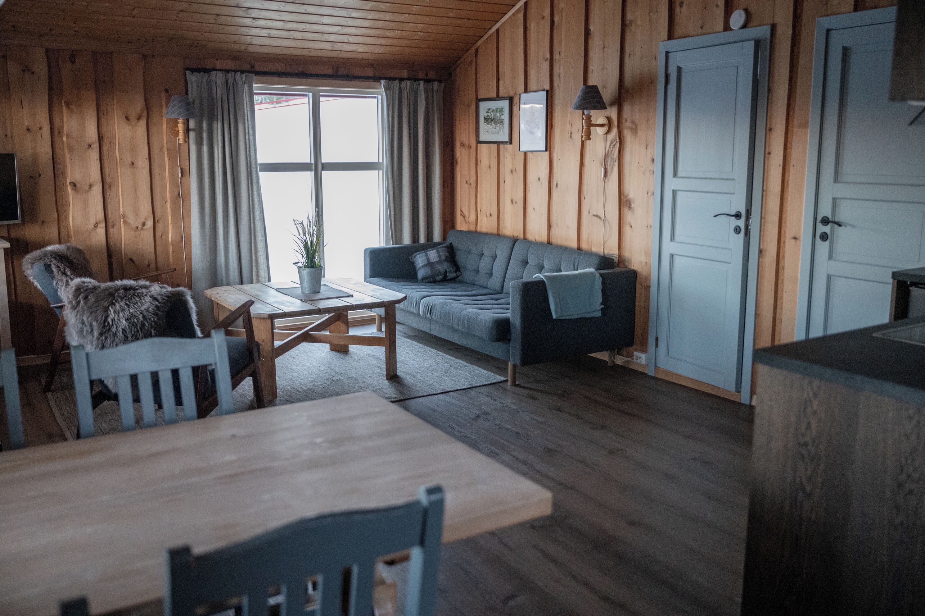 Una habitación acogedora con paredes de madera, un sofá gris, una mesa de comedor de madera y una silla con una manta de piel.