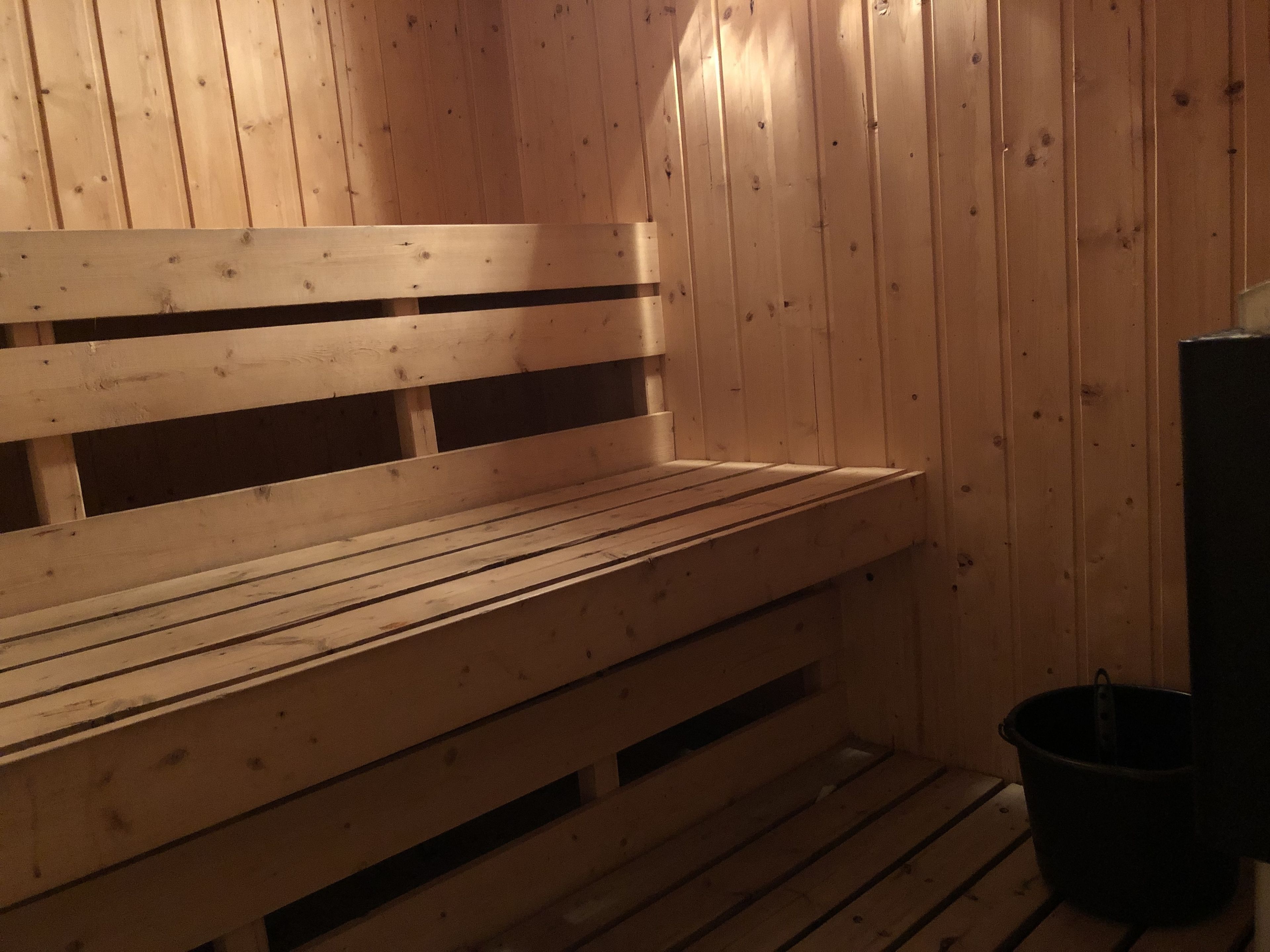 En träbänk i en bastu, med ribbformade ryggstöd och en svart hink på golvet.
