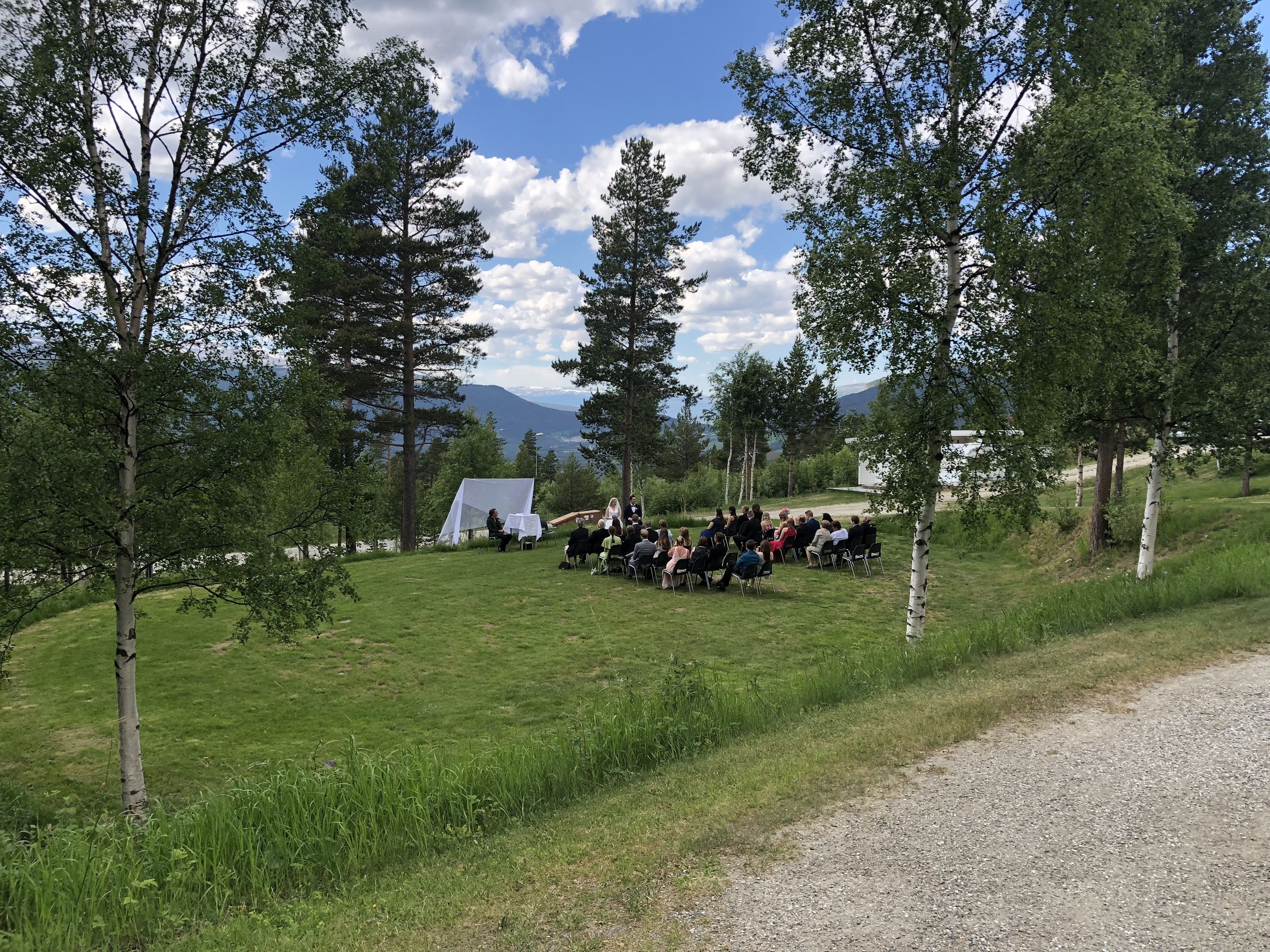 Un grupo de personas sentadas al aire libre en un área cubierta de césped, con árboles y una tienda de campaña al fondo.