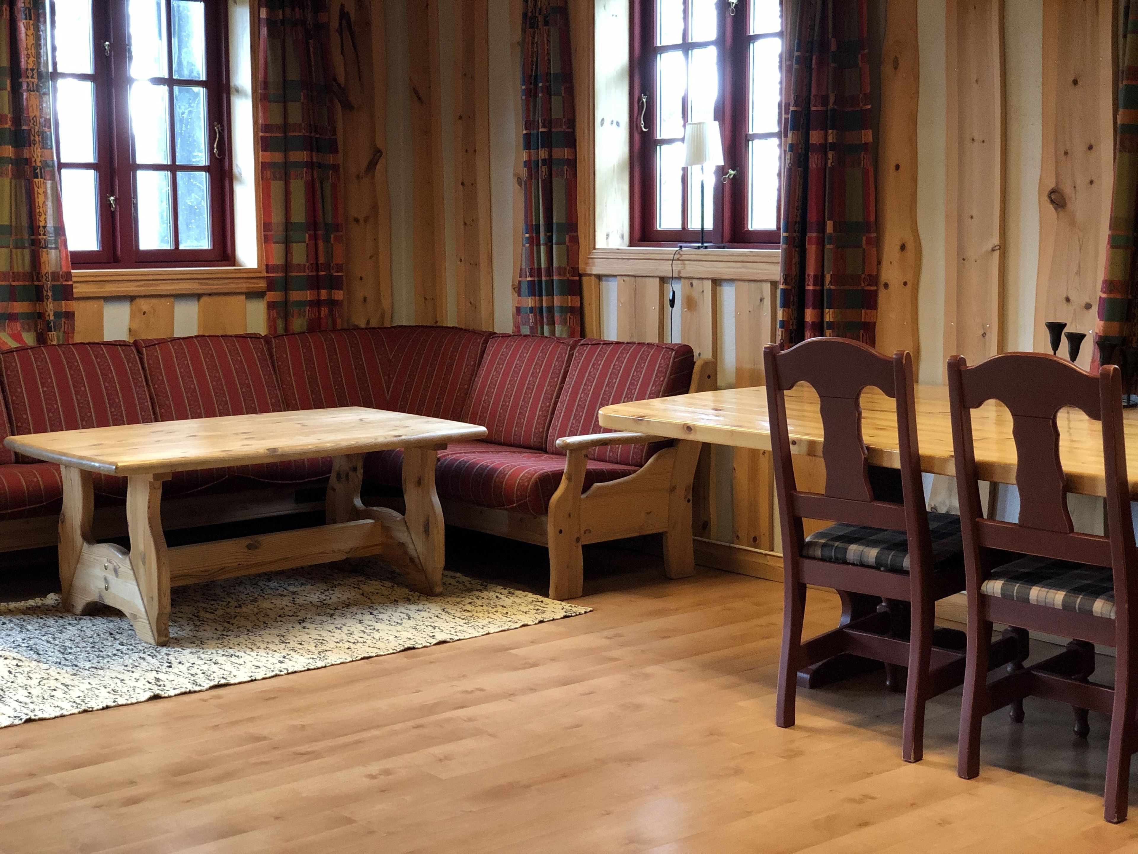 Una habitación acogedora con piso de madera, un sofá a rayas rojas, una mesa de madera y una silla de madera.